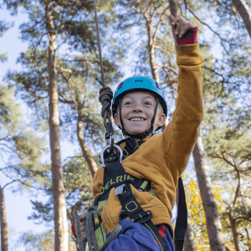Young person on a high rope activity in the forest smiling and pointing up