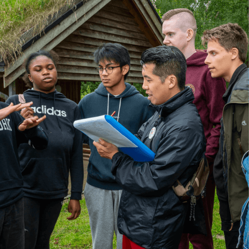 Group of young people stood in the forest around a clipboard - they are all in discussion