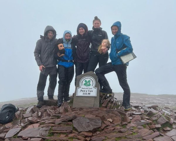 Group of apprentices stood at trig point on pen y fan in the rain wearing jackets