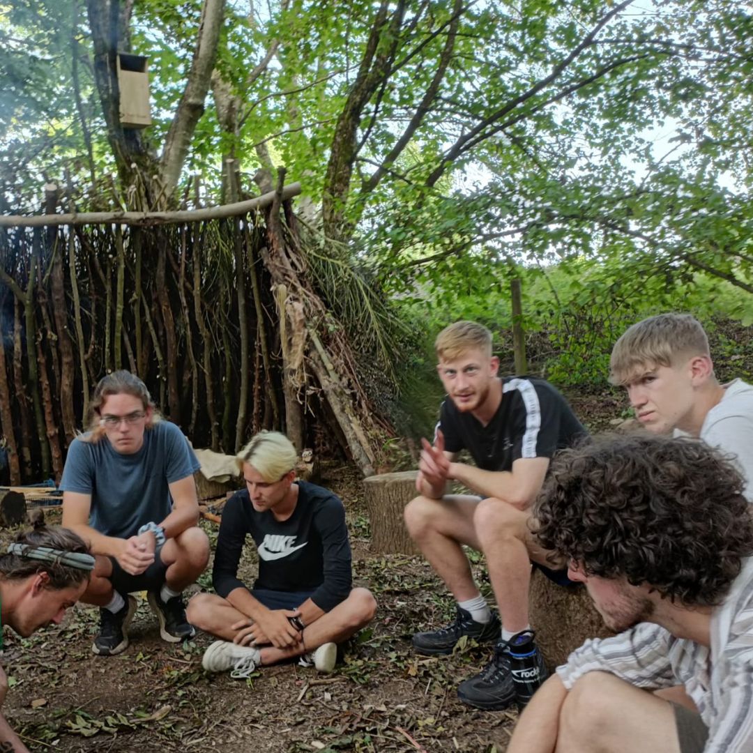 Avon tyrrell apprentices sat and knelt around a camp fire in the forest