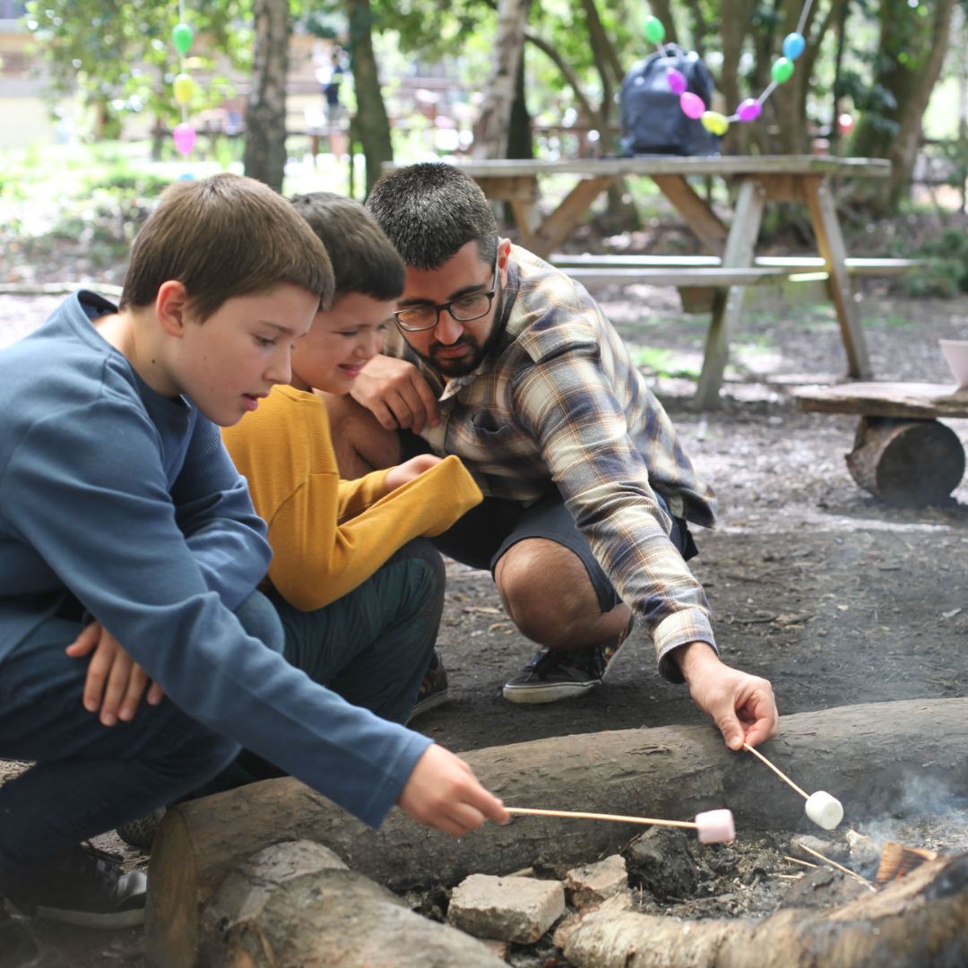 Two boys and man roasting marshmallows over a fire in the forest
