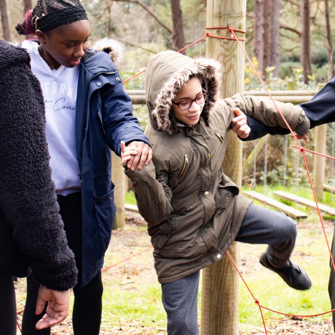 Young people in a line holding arms going through a roped spiders net doing a challenge