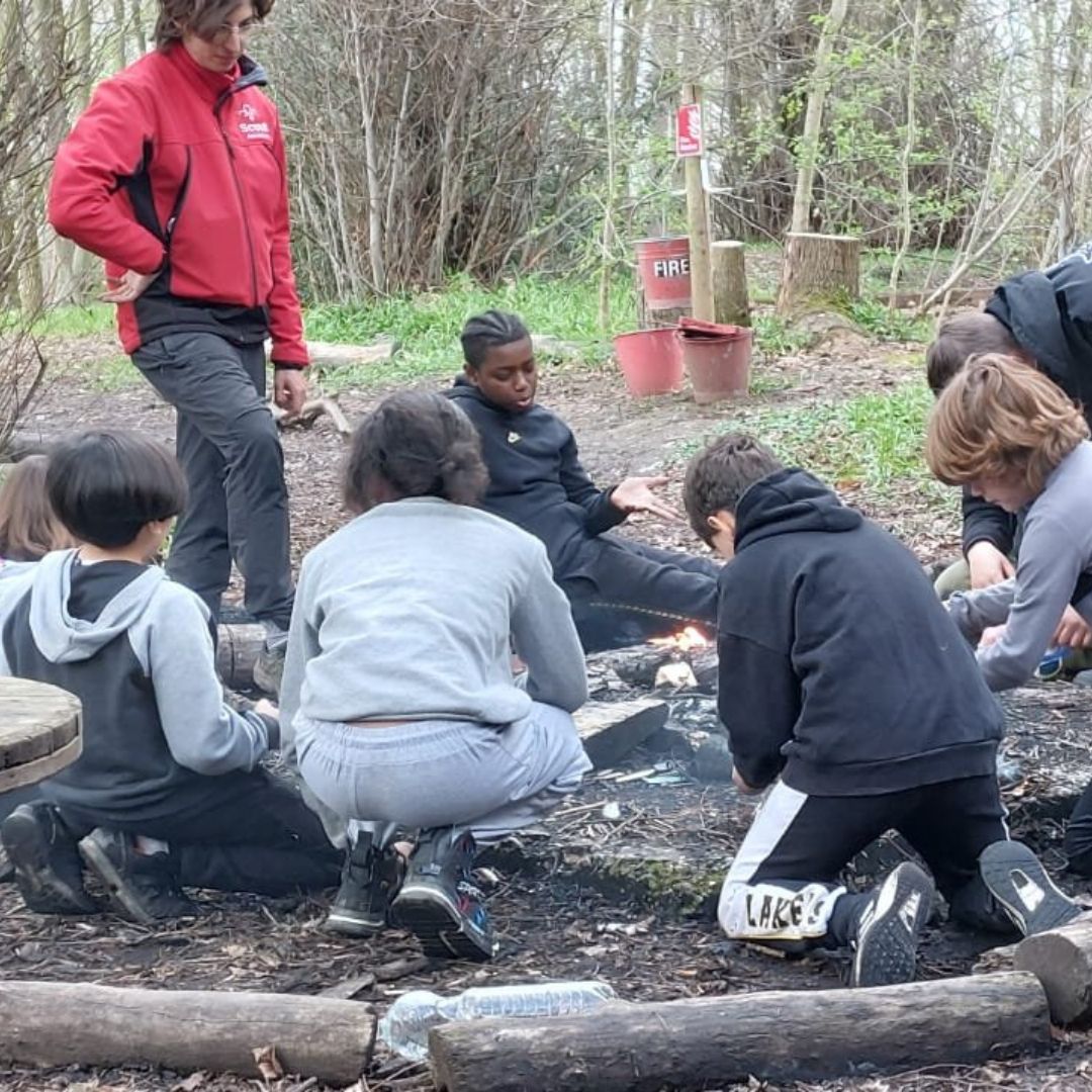 Group of people sat around a fire making the fire bigger