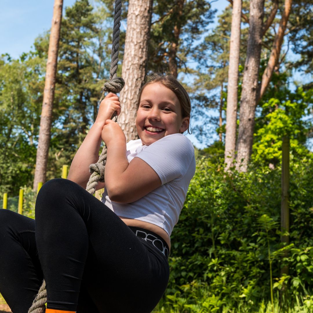 girl on small rope swing, swinging and smiling to camera