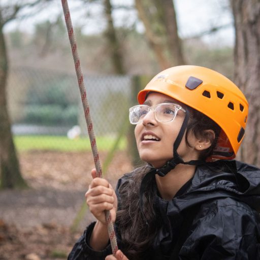 Young girl wearing a helmet and glasses pulling on a rope in the forest