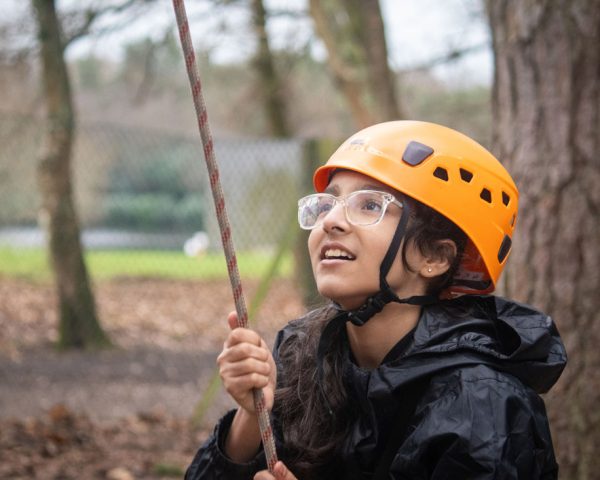 Young girl wearing a helmet and glasses pulling on a rope in the forest