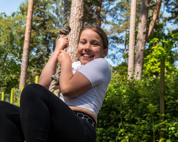 Young girl on a rope swing swiming to the camera in the forest