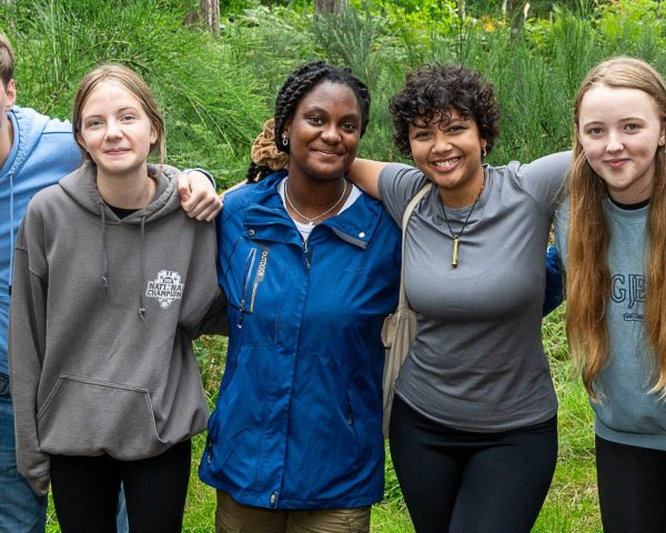 Group of young people stood in the forest in front of bushes with arms around shoulders smiling