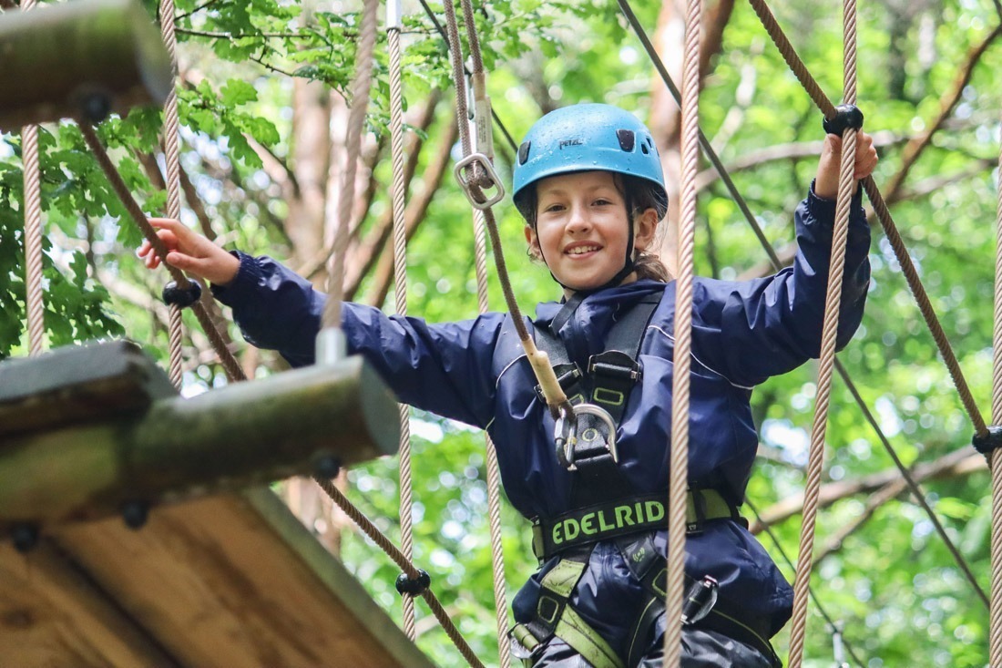 Young person on a tree top trail platform high in the trees wearing harness and helmet