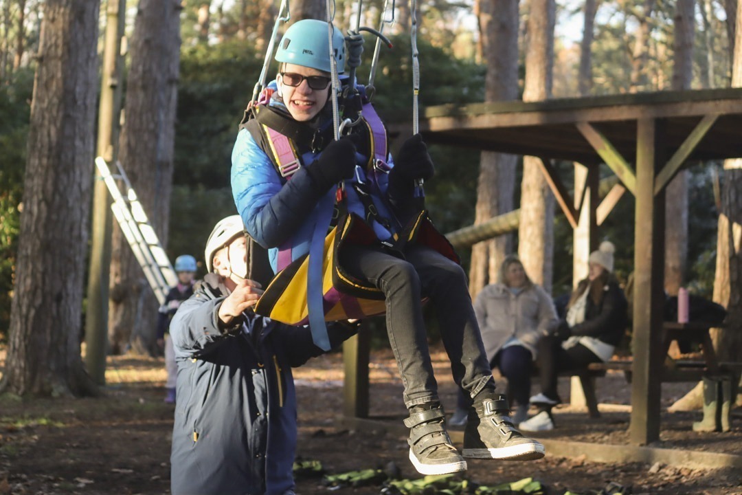 Young person in accessible harness seat raised above ground doing a high rope activity