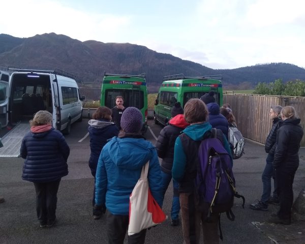 people stood in a car park with hills in the background in front of accessible mini buses