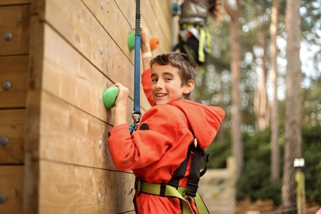 boy wearing orange hoodie doing the climbing wall with harness at avon tyrell