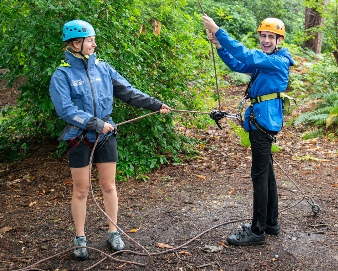Boy with female instructor on a belay system for high ropes smiling to camera in the forest
