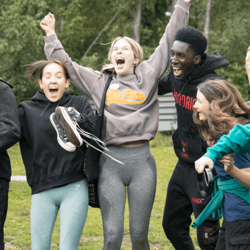 Group of young people smiling and cheering with arms in air in the forest at avon tyrrell outdoor centre