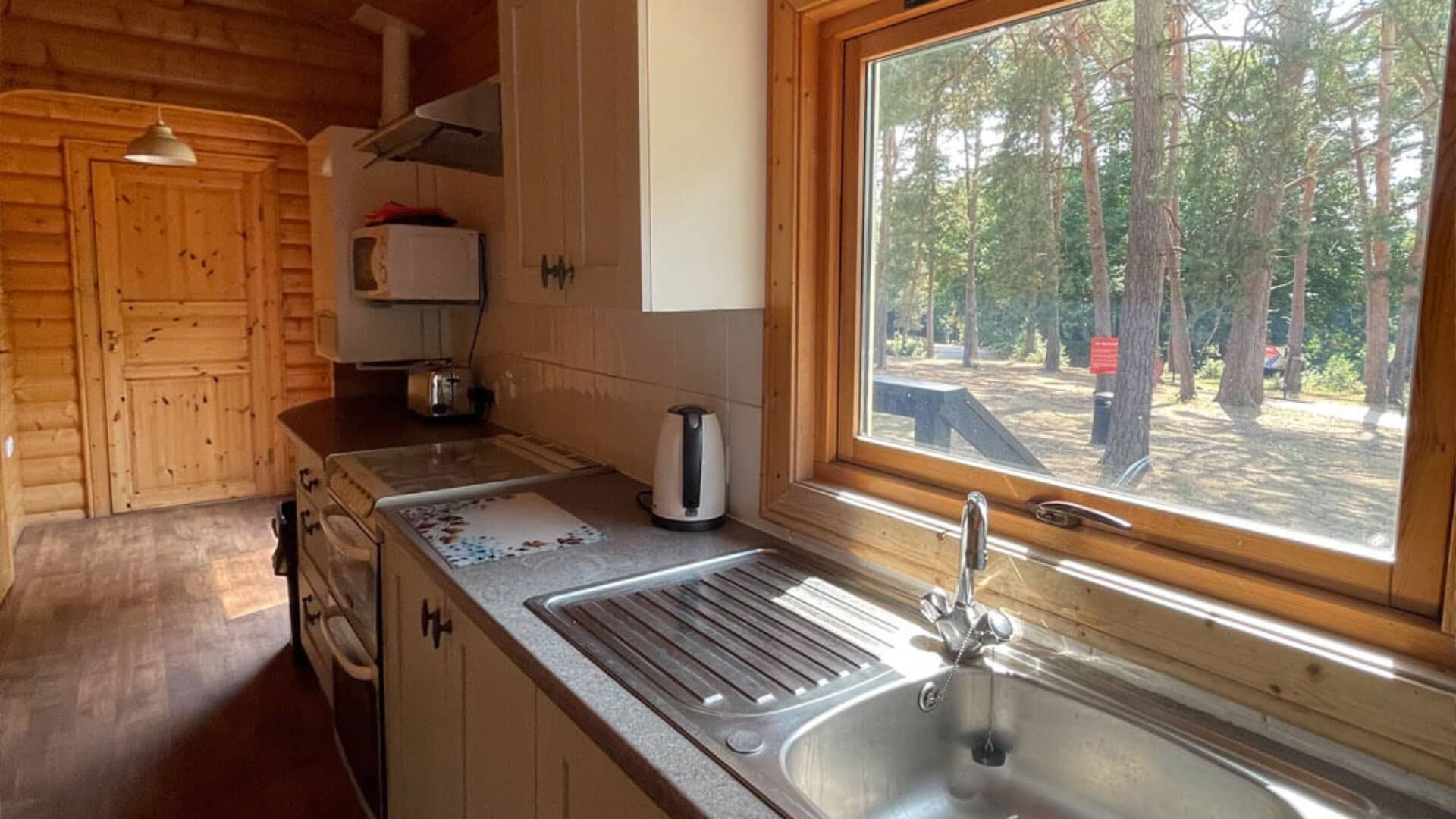 Kitchen area with sink, cooker microwave, boiler, and a window looking out onto the forest at Avon Tyrell in the forest lodges
