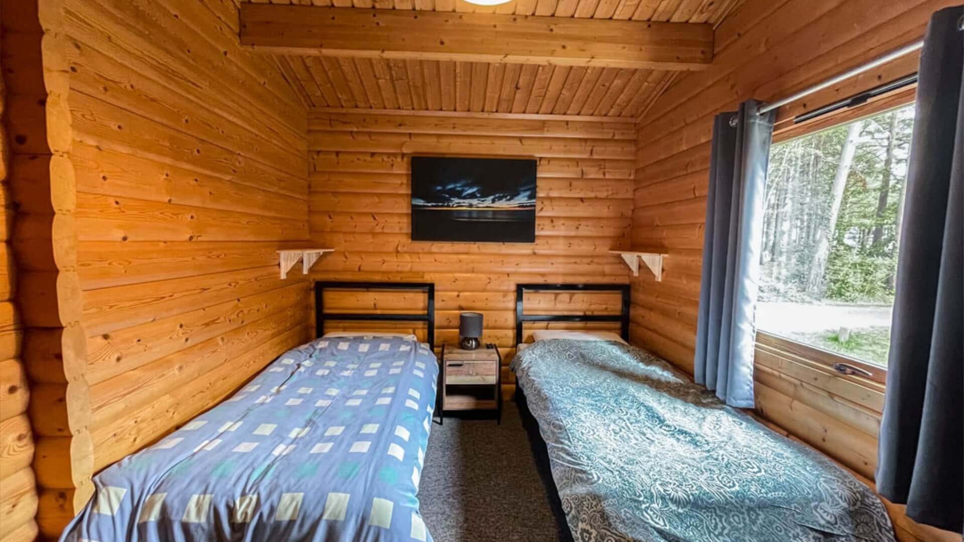 two single twin beds in a wooden forest lodge with mini lamp on a bedside table