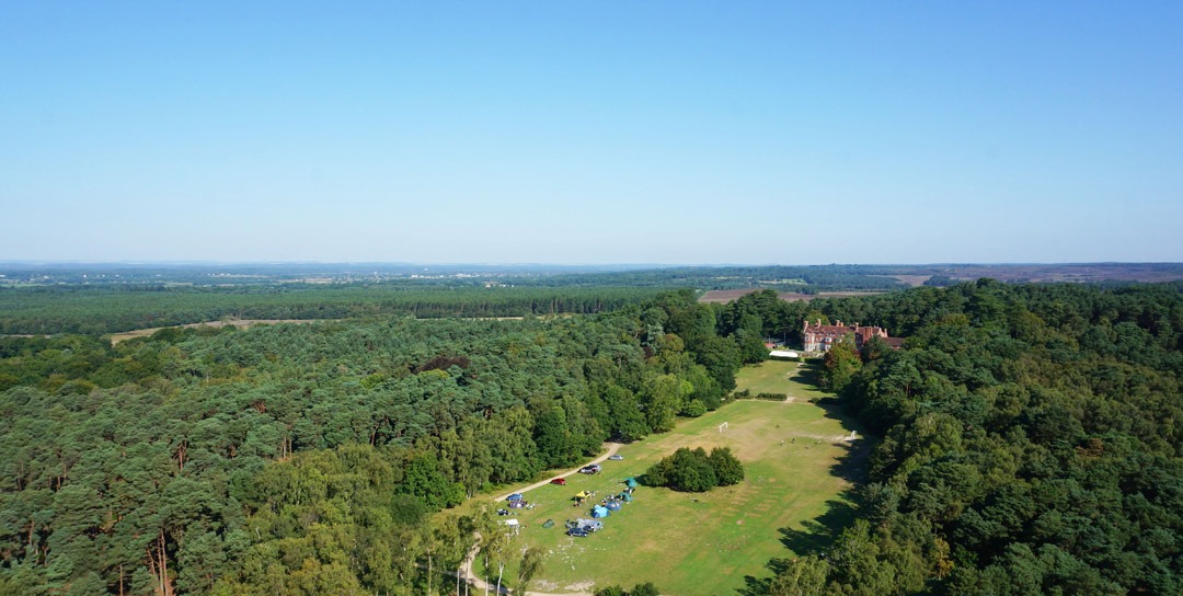 Aerial image shot on a drone of Avon Tyrrell's manor house in the New Forest - the manor house sits on a large forest site with trees and grass areas surronding it with tents out for campers