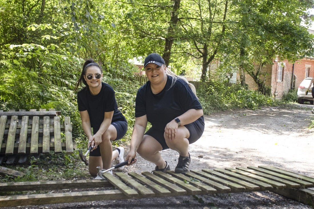 Two adults doing some volunteering gardening working on a wooden fence in the forest at avon tyrrell