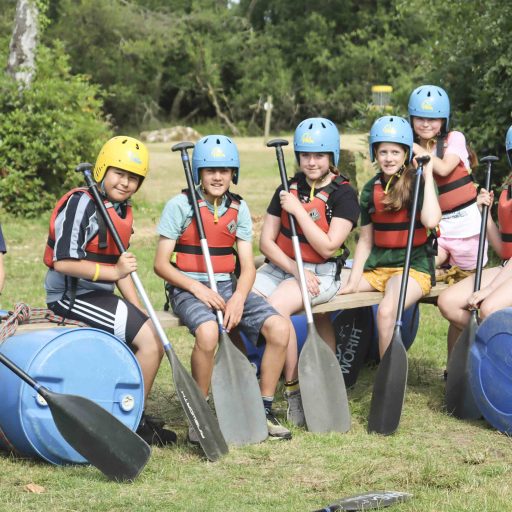 young people on a raft wearing life jackets and helmets smiling to camera