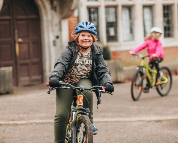 Young person cycling bike in front of a manor house on gravel floor with young person out of focus cycling bike behind