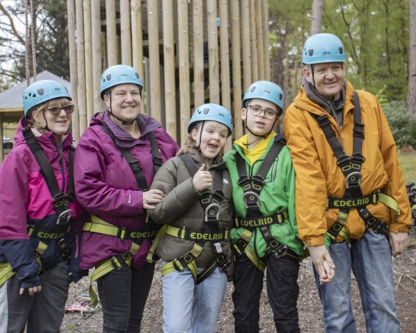 family group smiling to camera in front of Avon tyrrells zip wire tower wearing harnesses and helmets
