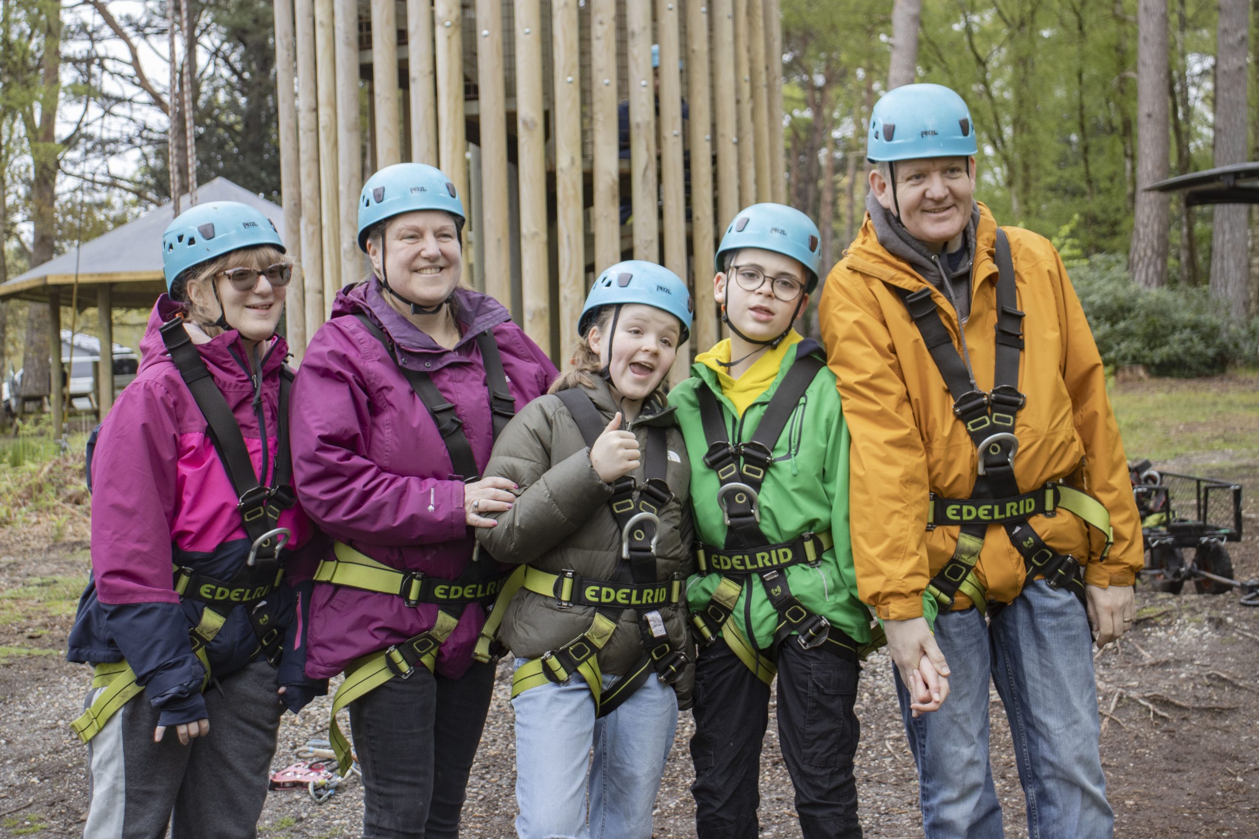 family group smiling to camera in front of Avon tyrrells zip wire tower wearing harnesses and helmets