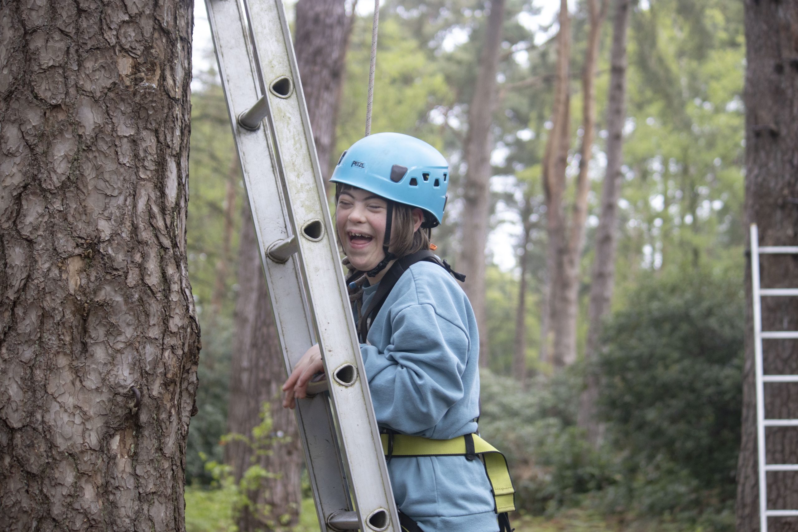 young person with SEND smiling to camera on a ladder doing high ropes in the new forest at Avon Tyrrell
