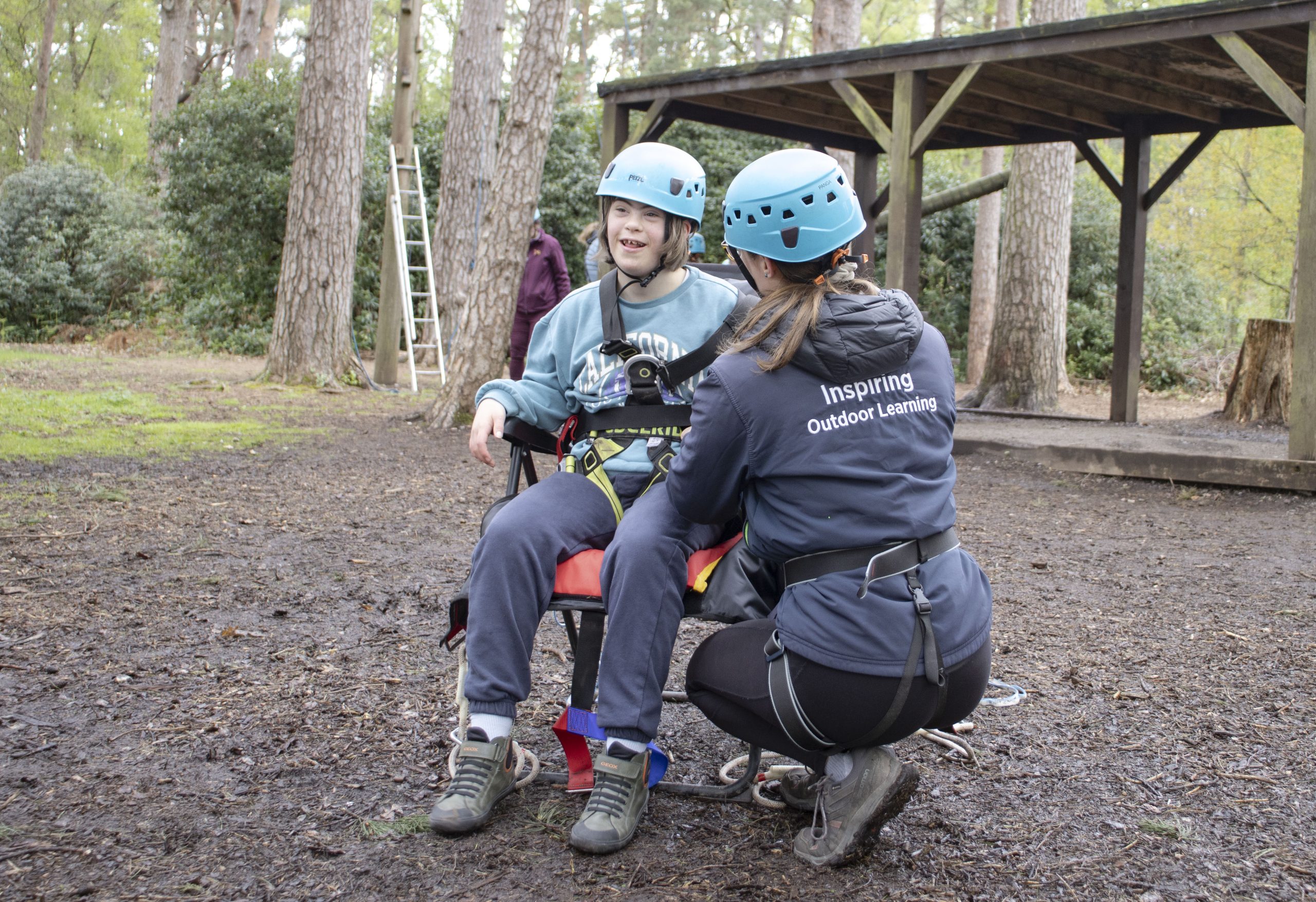 young person and Avon tyrrell instructor getting young person wearing helmet into specialised SEND harness for high ropes in the new forest