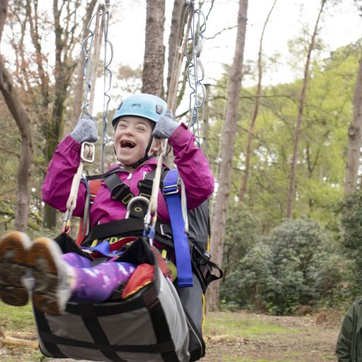 SEND young person on specialised harness doing high ropes smiling