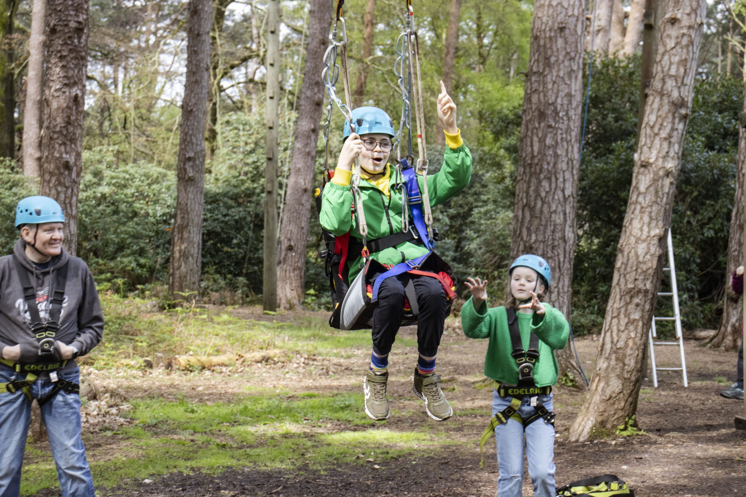 young person boy in specialised harness with siblings swinging him in seat doing high ropes in the forest