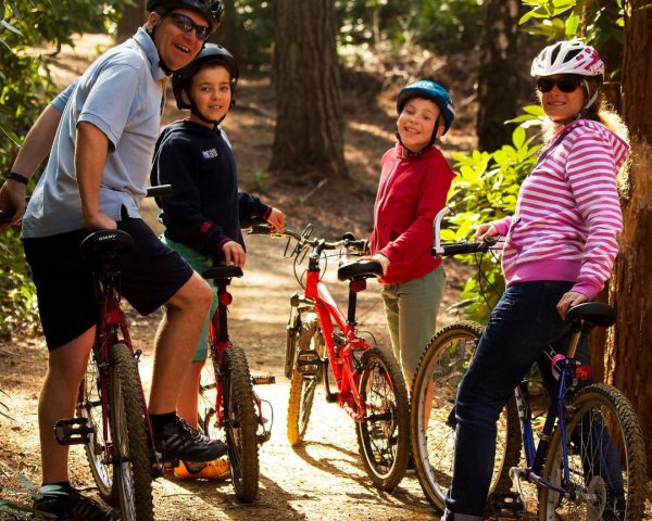 family on bikes with mum and dad smiling and two boys miling behind them ready for a bike ride in the forest wearing helmets