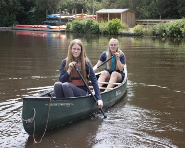 Young person and instructor wearing life jackets in a canoe on a lake in the forest smiling to camera