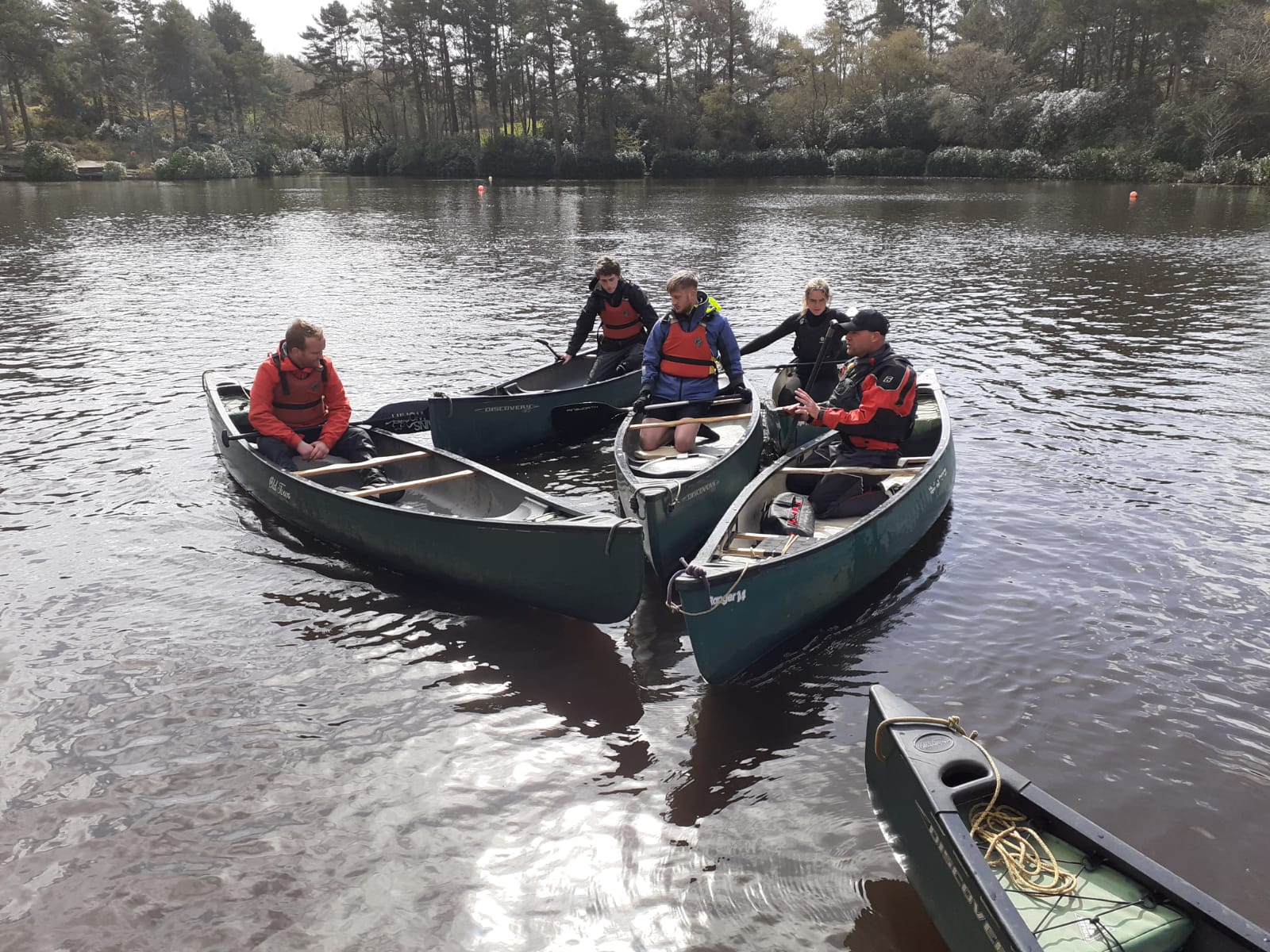 apprentices on open canoes on a lake in the new forest smiling to camera learning about paddle techniques and