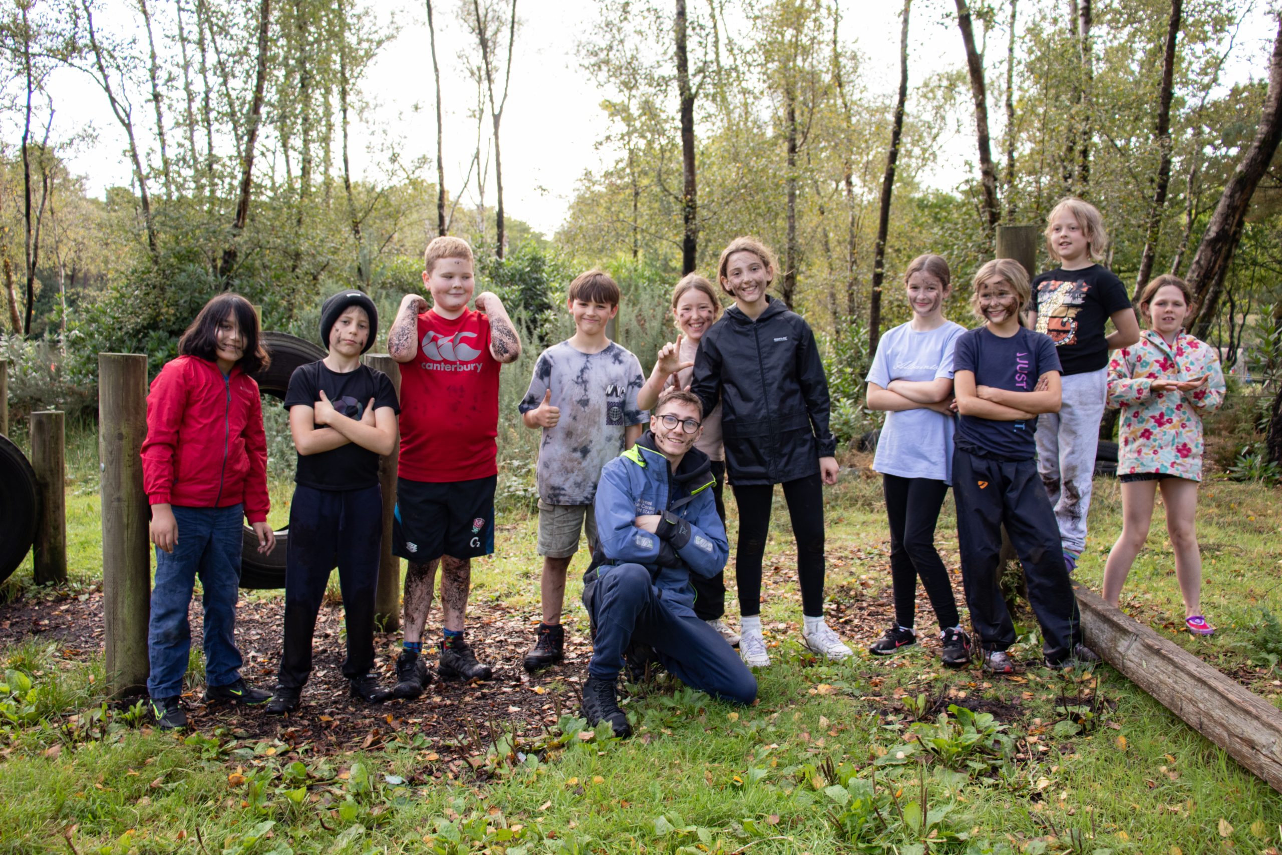 Group of young people siming to camera stood in a straight line with instructor sat in front posing. Image was taken in the New Forest with trees in the background on a winters day